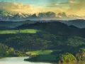 Krajobraz jak z najpopularniejszych parków narodowych w Polsce: jezioro, zielone wzgórza, lasy i ośnieżone szczyty Tatr w oddali.