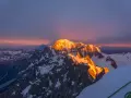 Mont Blanc latem, oświetlony złotym blaskiem wschodu słońca, z cieniem góry rzucającym się na niebo.