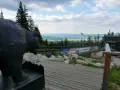 Pomnik niedźwiedzia na tle panoramy Tatr poza szlakiem. Drewniana kładka prowadzi do budynku z widokiem na dolinę.