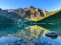 Idealny weekend w Tatrach: Morskie Oko odbija skaliste szczyty i zielone zbocza. Czysta woda odsłania kamienie.
