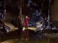 Eksplorator w jaskini, zanurzony po kolana w wodzie, odkrywa tajemnice speleologii. Stalagmity i nacieki tworzą niezwykły krajobraz.