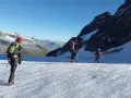Trzej alpiniści na lodowcu, uczący się jak zostać przewodnikiem górskim. W tle majestatyczne szczyty.