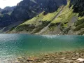 Turkusowe jezioro w Tatrach, niedaleko Zakopanego, otoczone stromymi, zielonymi zboczami gór.