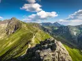 Szlak turystyczny wije się po zielonych zboczach, prowadząc w stronę Kasprowego Wierchu. W oddali widać kolejne pasma górskie Tatr.