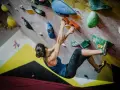 Kobieta wspina się po kolorowej ścianie, szukając chwytów. To właśnie bouldering – sportowa wspinaczka bez liny, na niskich ścianach.