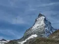 Widok na ośnieżony szczyt Matterhornu, z paralotnią szybującą na błękitnym niebie. To jak wejście na Mont Blanc dla odważnych.