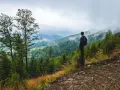 Mężczyzna z plecakiem podziwia mglisty górski krajobraz. To właśnie jest trekking – odkrywanie natury pieszo.
