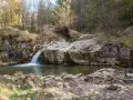 Mały wodospad w potoku, gdzie biała woda Szczawnica spływa po kamieniach. Wokół las i skały.