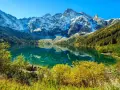 Turkusowe Morskie Oko odbija ośnieżone szczyty Tatr. Jesienne drzewa otaczają taflę wody.