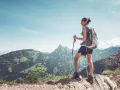 Młoda kobieta z plecakiem i kijkami trekkingowymi podziwia górski krajobraz. Pokazuje, jak chodzić z kijkami trekkingowymi, by czerpać radość z wędrówki.