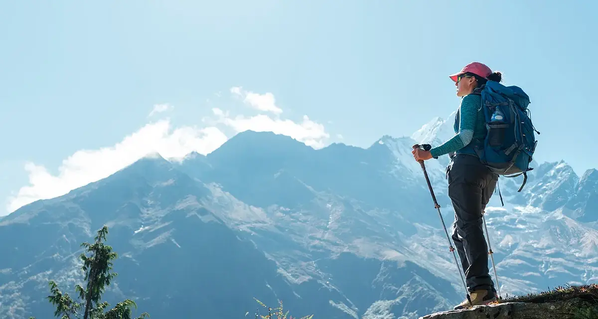 Kobieta z plecakiem i kijkami trekkingowymi podziwia majestatyczne góry w drodze na mount everest base camp.