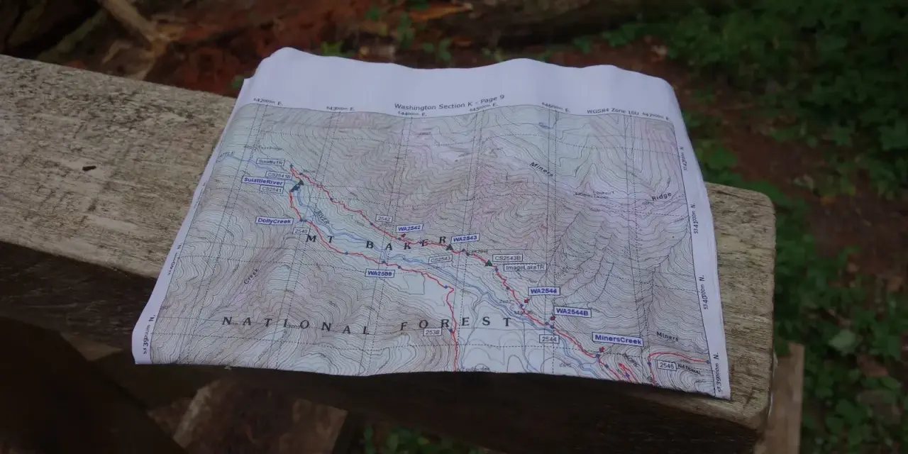 Mapa szlaku grzbietu pacyficznego z zaznaczonymi punktami i rzekami, leżąca na drewnianej ławce.