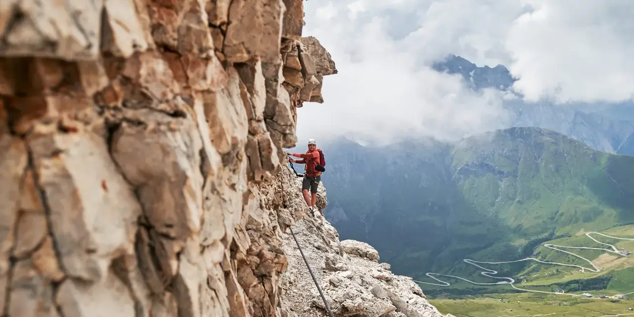 Wspinacz na via ferraty w Dolomitach, z widokiem na kręte drogi w dolinie.