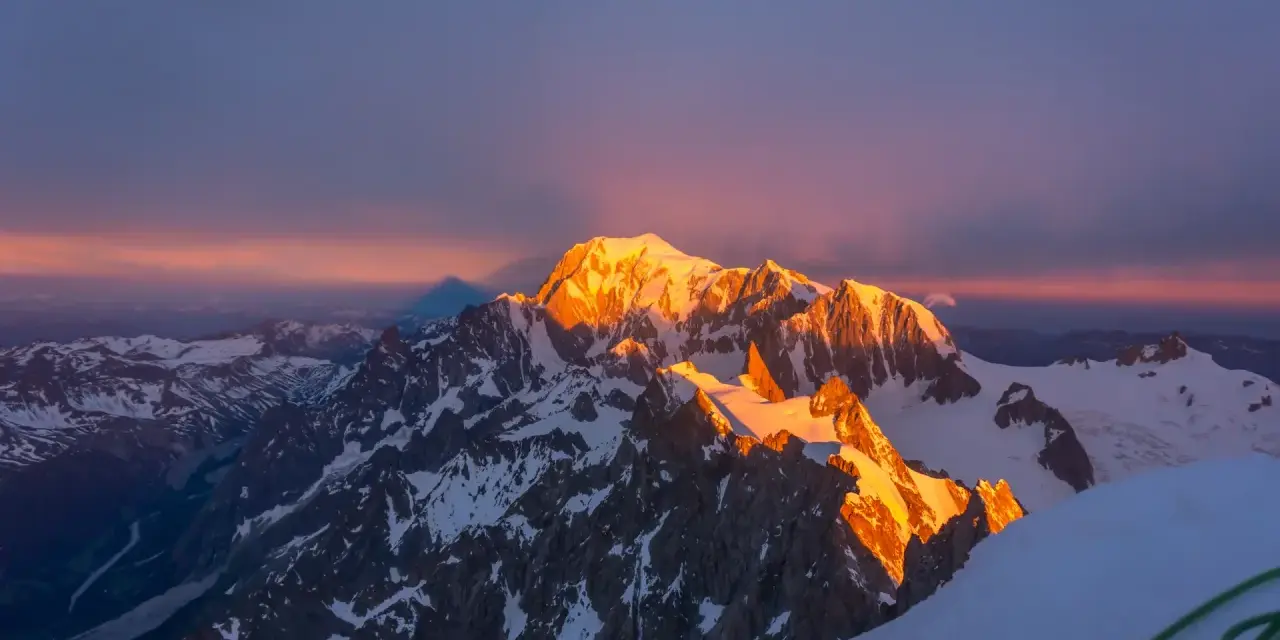 Mont Blanc latem, oświetlony złotym blaskiem wschodu słońca, z cieniem góry rzucającym się na niebo.