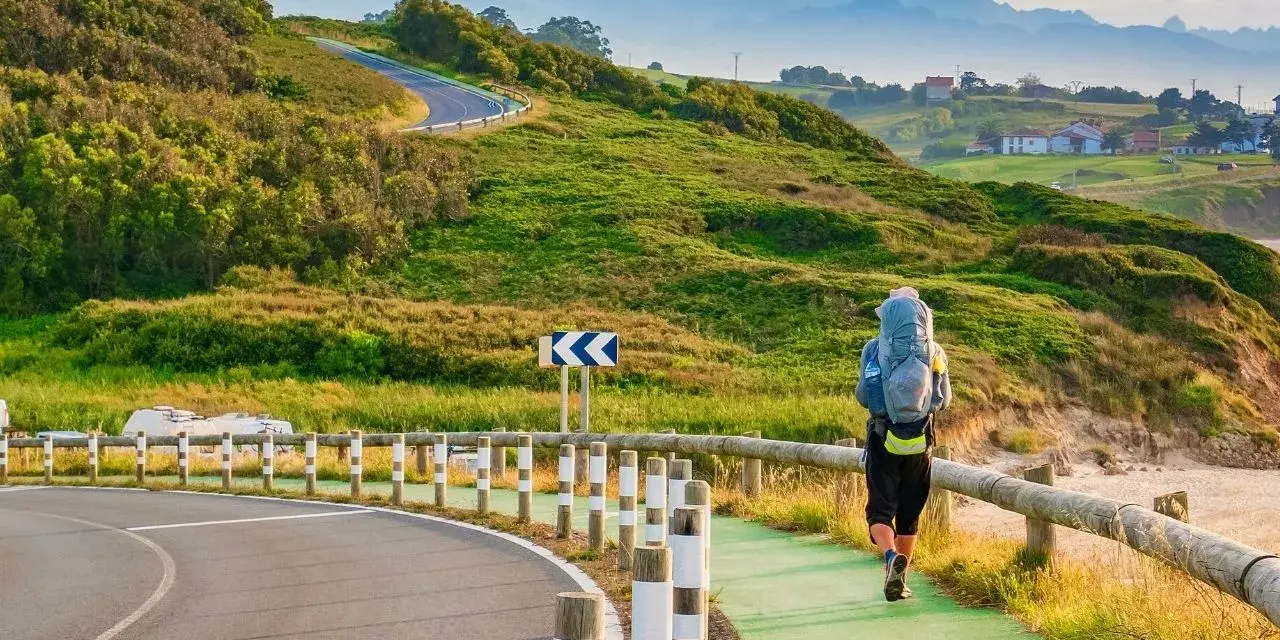 Pielgrzym z plecakiem idzie ścieżką wzdłuż wybrzeża, jedną z wielu tras Camino de Santiago.