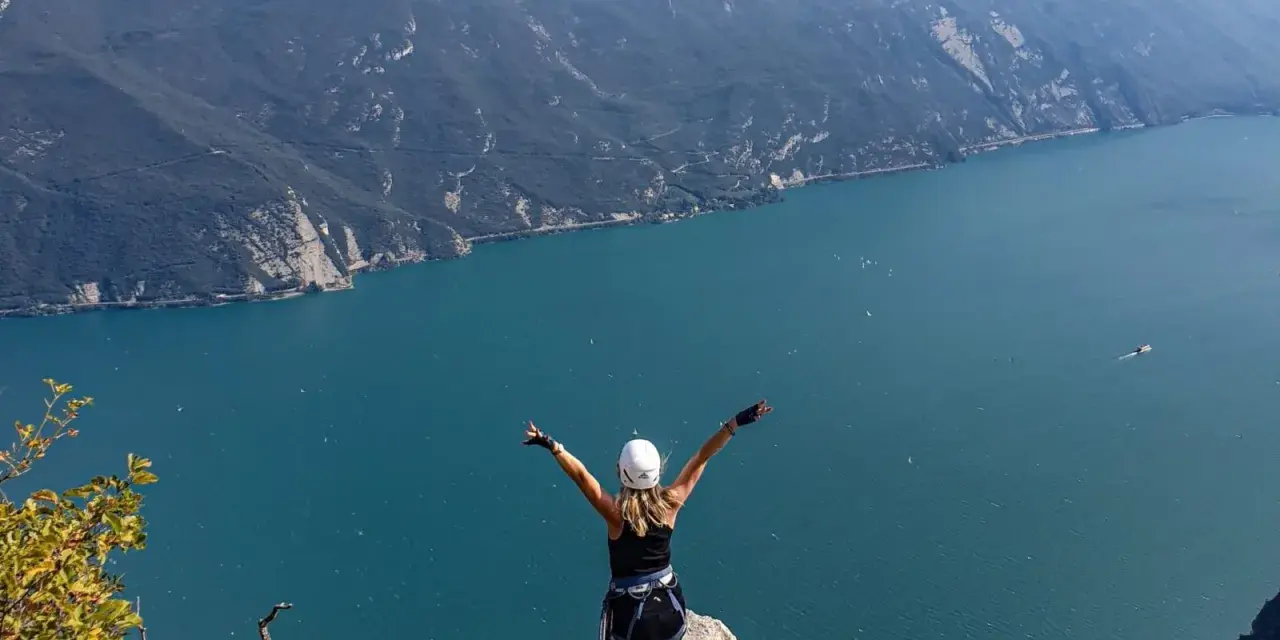 Kobieta w kasku i uprzęży cieszy się widokiem na jezioro Garda po pokonaniu via ferrata.