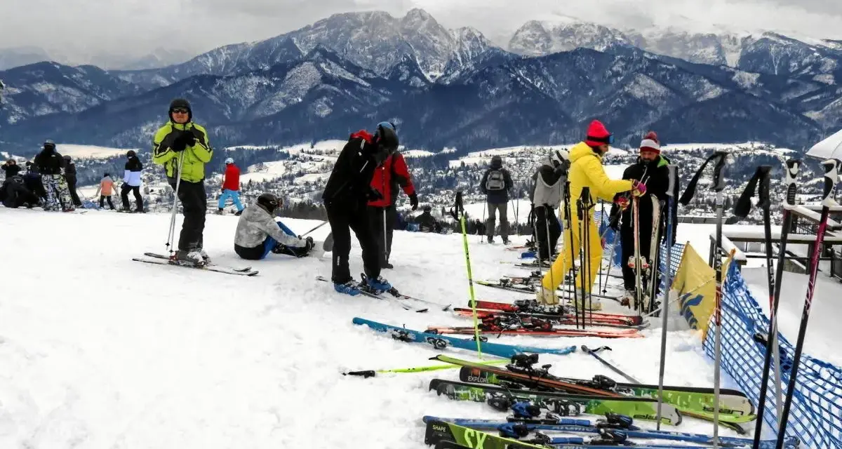 Ludzie na nartach i snowboardach na stoku, w tle góry. Zastanawiasz się, ile się idzie na Gubałówkę? Tu jest zimowo i aktywnie!