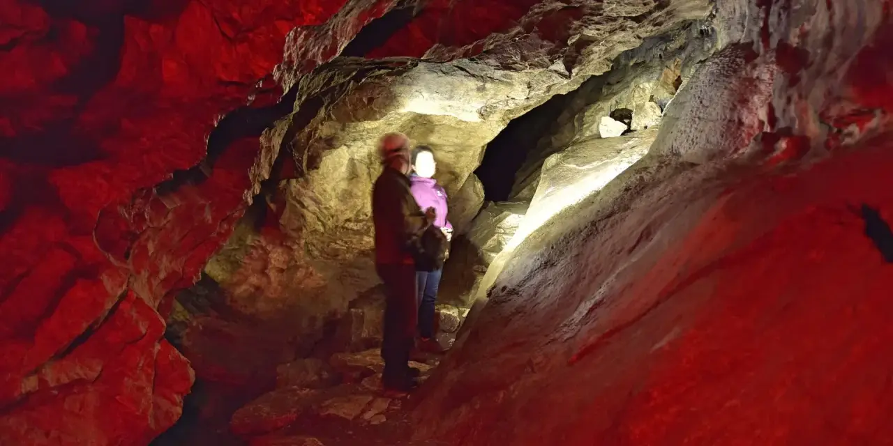Para zwiedza jaskinie do zwiedzania w Polsce. Czerwone światło podkreśla surowe piękno skalnych formacji.