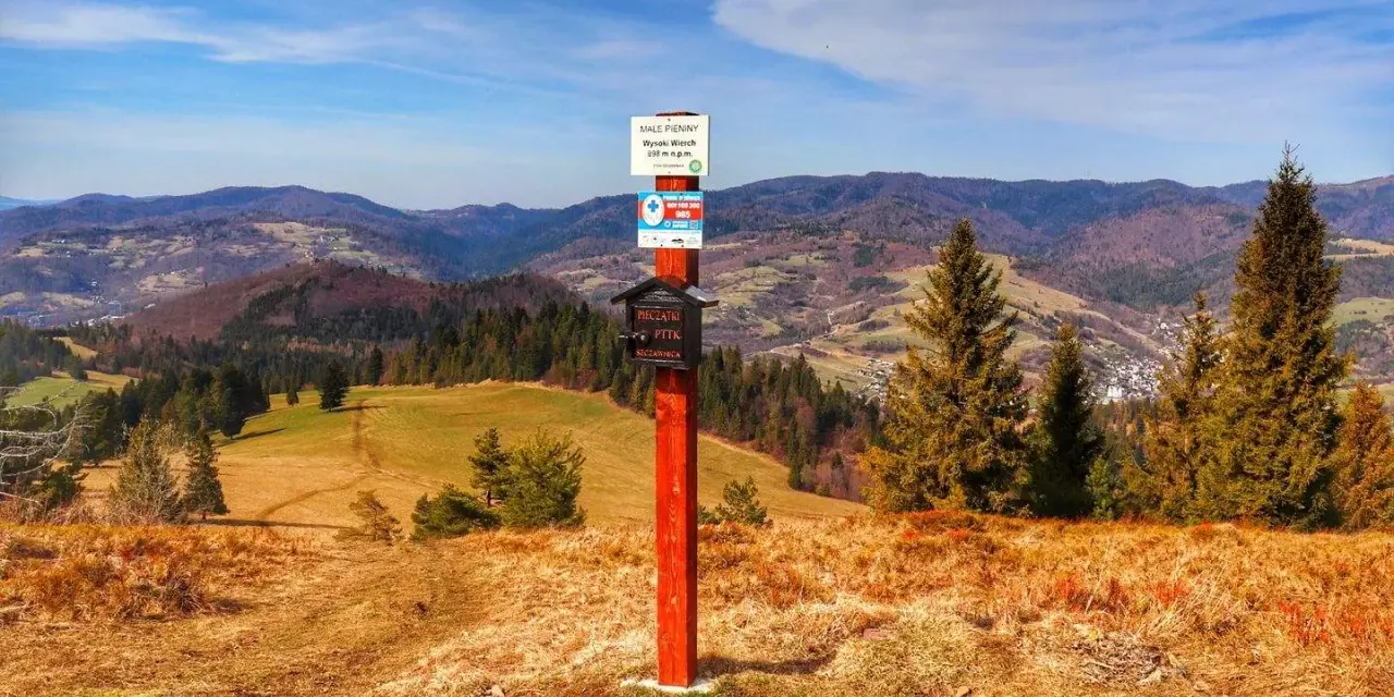Wysoki Wierch w Pieninach, szlak turystyczny z tabliczką i skrzynką na pieczątki. W tle malownicze wzgórza i lasy.