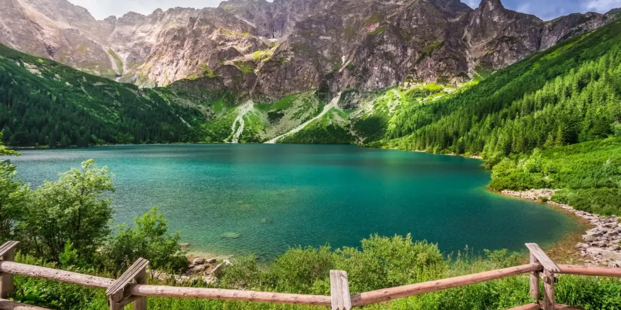 Turkusowe jezioro otoczone zielonymi zboczami gór i lasem, przypominające beskidzkie Morskie Oko.