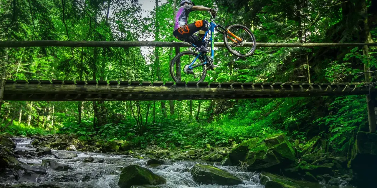 Rowerzysta wykonuje trik na drewnianym moście nad potokiem. Wspaniałe trasy rowerowe Zakopane czekają na odkrycie!