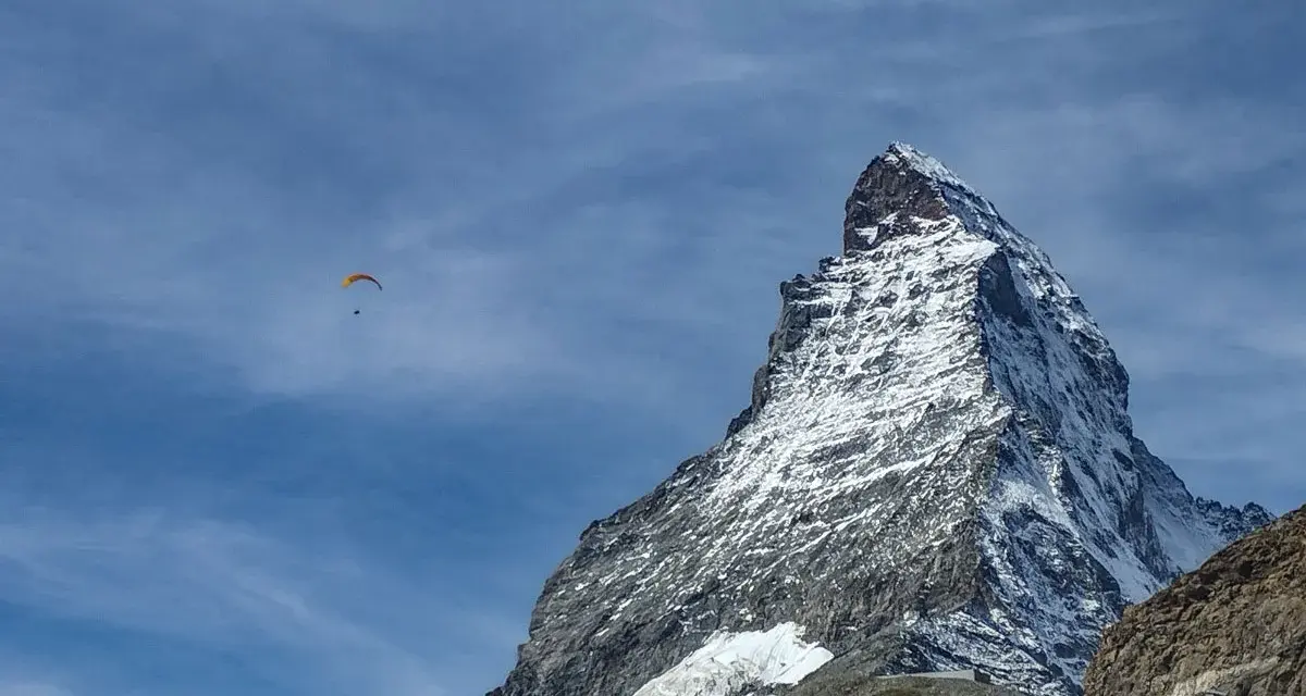 Widok na ośnieżony szczyt Matterhornu, z paralotnią szybującą na błękitnym niebie. To jak wejście na Mont Blanc dla odważnych.