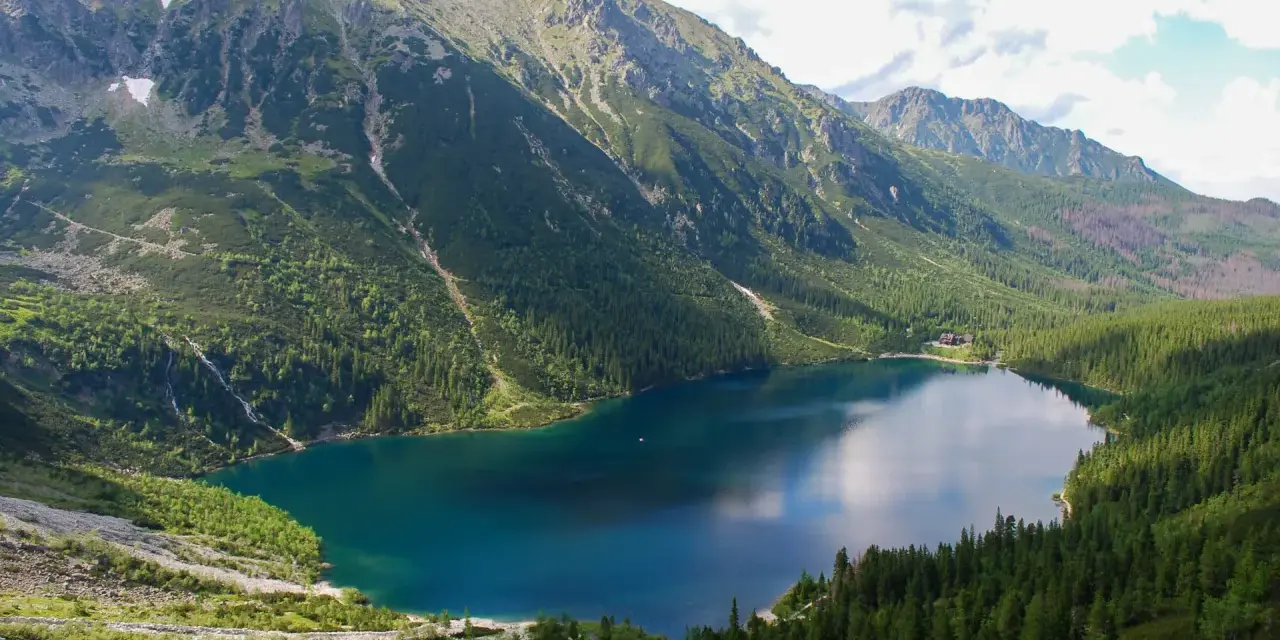 Największe jezioro w Tatrach, Morskie Oko, otoczone zielonymi lasami i skalistymi szczytami.