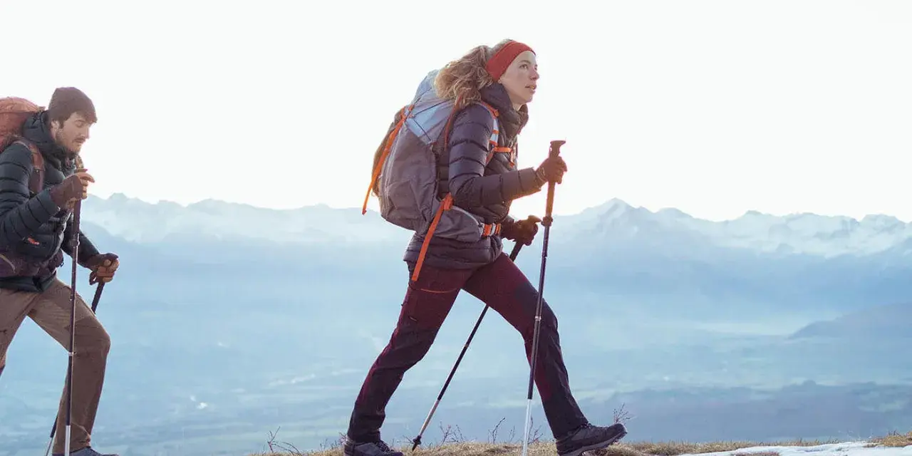 Para, co to jest hiking? To dwójka ludzi z plecakami i kijkami, idących po ośnieżonym szlaku w górach.