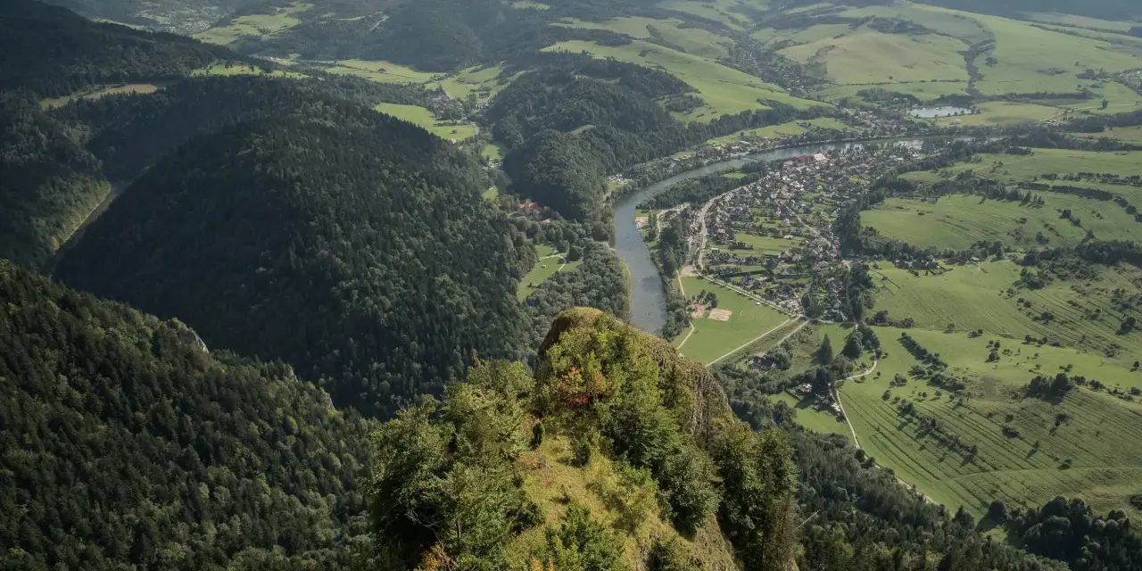 Widok z Trzech Koron na Szczawnicę i Dunajec. Góry Pieniny w zieleni, malownicza dolina rzeki i miasteczko.