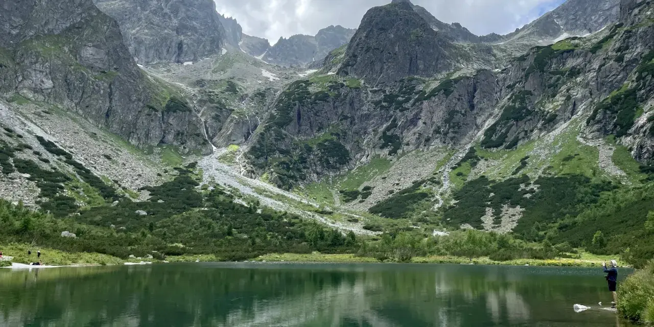 Piękne szlaki na Słowacji. Jezioro w górach odbija skaliste szczyty i zielone zbocza.