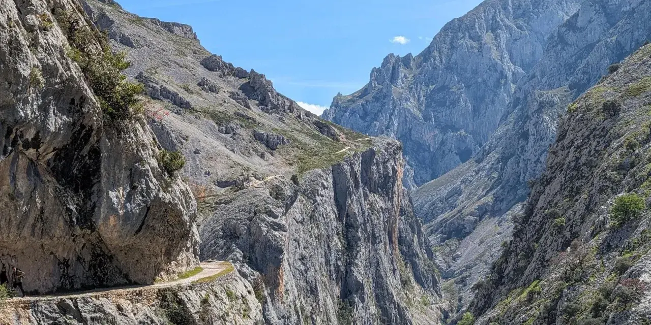 Wąska ścieżka wzdłuż skalnej ściany, część szlaku Ruta del Cares, prowadzi przez surowe, górskie krajobrazy.