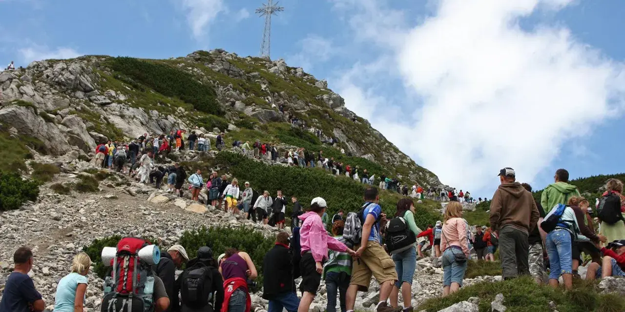 Tłum turystów podąża czerwonym szlakiem na Giewont. W oddali widoczny krzyż.