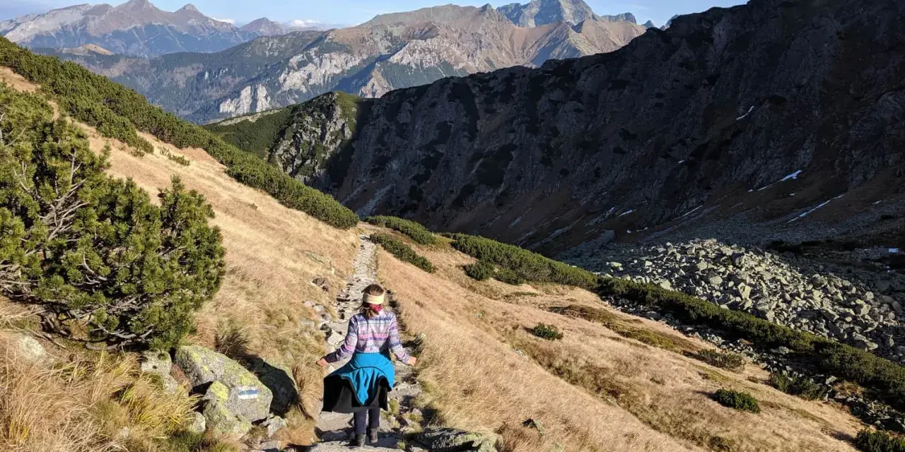 Osoba wędruje kamienistym szlakiem w Tatrach. Widok na góry i dolinę, idealne tatry szlaki dla średnio zaawansowanych.