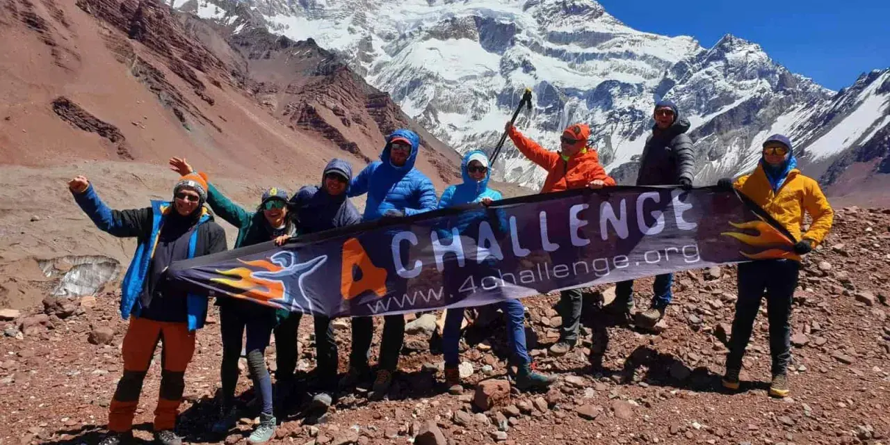Grupa zdobywców z banerem "4 CHALLENGE" na tle ośnieżonego Aconcagui, najwyższego szczytu Andów.