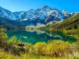 Turkusowe Morskie Oko odbija ośnieżone szczyty Tatr. Jesienne drzewa otaczają taflę wody.