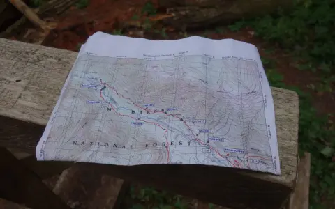 Mapa szlaku grzbietu pacyficznego z zaznaczonymi punktami i rzekami, leżąca na drewnianej ławce.