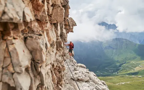 Wspinacz na via ferraty w Dolomitach, z widokiem na kręte drogi w dolinie.