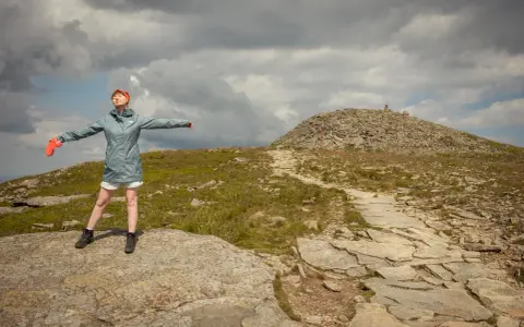 Kobieta z rękami rozłożonymi na boki na szczycie Babiej Góry, podążając czerwonym szlakiem.