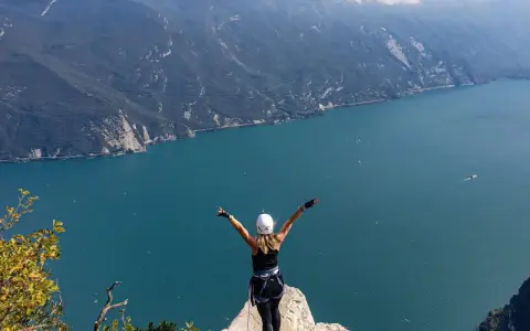 Kobieta w kasku i uprzęży cieszy się widokiem na jezioro Garda po pokonaniu via ferrata.