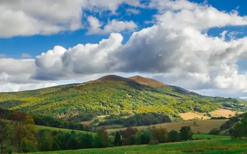 Bieszczady jakie to góry? Łagodne, zielone wzgórza pokryte lasami, z pojedynczymi szczytami i malowniczymi dolinami, pod błękitnym niebem z kłębiastymi chmurami.