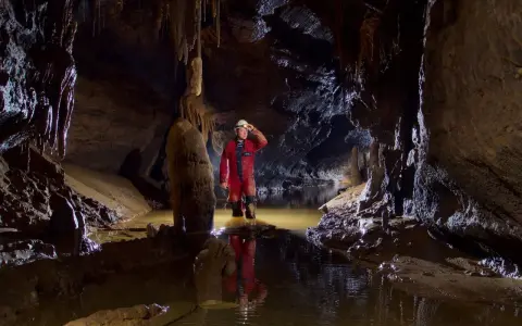 Eksplorator w jaskini, zanurzony po kolana w wodzie, odkrywa tajemnice speleologii. Stalagmity i nacieki tworzą niezwykły krajobraz.