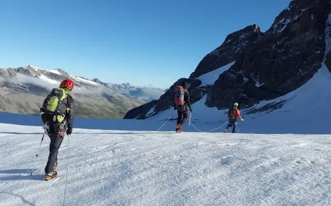 Trzej alpiniści na lodowcu, uczący się jak zostać przewodnikiem górskim. W tle majestatyczne szczyty.