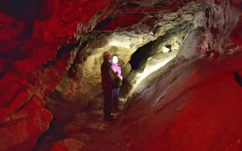 Para zwiedza jaskinie do zwiedzania w Polsce. Czerwone światło podkreśla surowe piękno skalnych formacji.