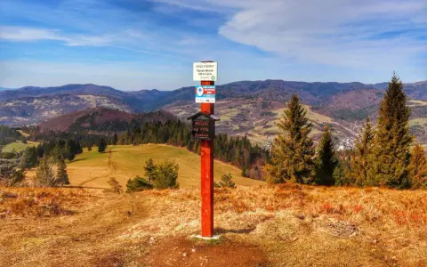 Wysoki Wierch w Pieninach, szlak turystyczny z tabliczką i skrzynką na pieczątki. W tle malownicze wzgórza i lasy.