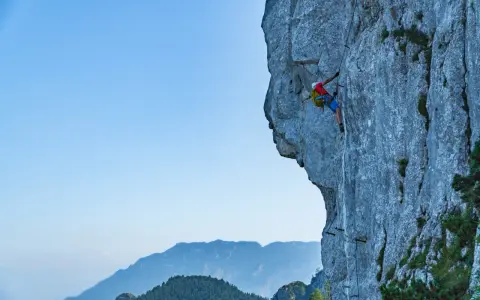 Wspinacz pokonuje via ferrata niemcy, zmagając się z pionową ścianą skalną. W tle piękne góry.