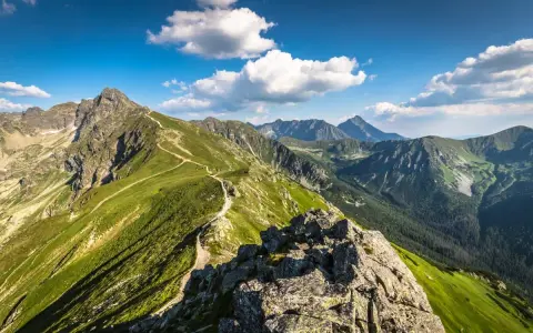 Szlak turystyczny wije się po zielonych zboczach, prowadząc w stronę Kasprowego Wierchu. W oddali widać kolejne pasma górskie Tatr.