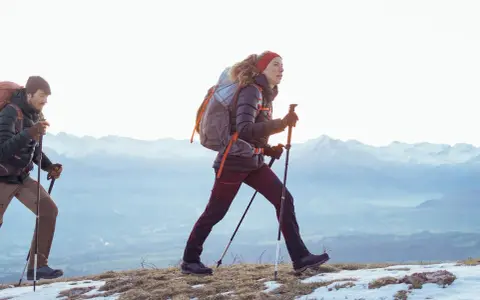 Para, co to jest hiking? To dwójka ludzi z plecakami i kijkami, idących po ośnieżonym szlaku w górach.