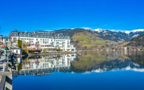 Grand Hotel nad jeziorem w Zell am See, z odbiciem w spokojnej wodzie i ośnieżonymi górami w tle.