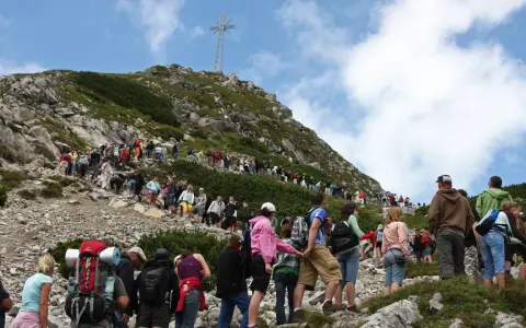 Tłum turystów podąża czerwonym szlakiem na Giewont. W oddali widoczny krzyż.