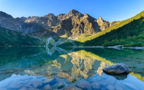Morskie Oko jesienią. Lśniąca tafla jeziora odbija skaliste szczyty Tatr i zielone lasy.
